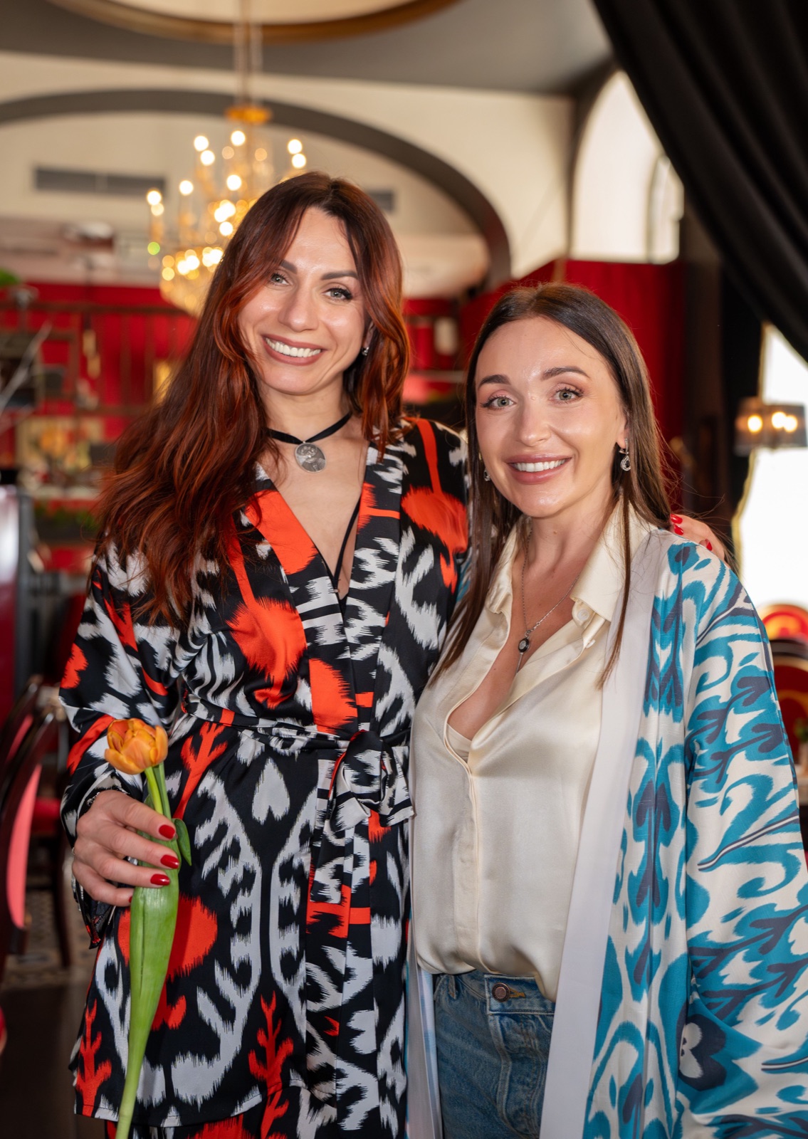 Two women in red and turquoise ikat coats with tulips at a Vienna fashion event — event photography by Best Alex Shots
