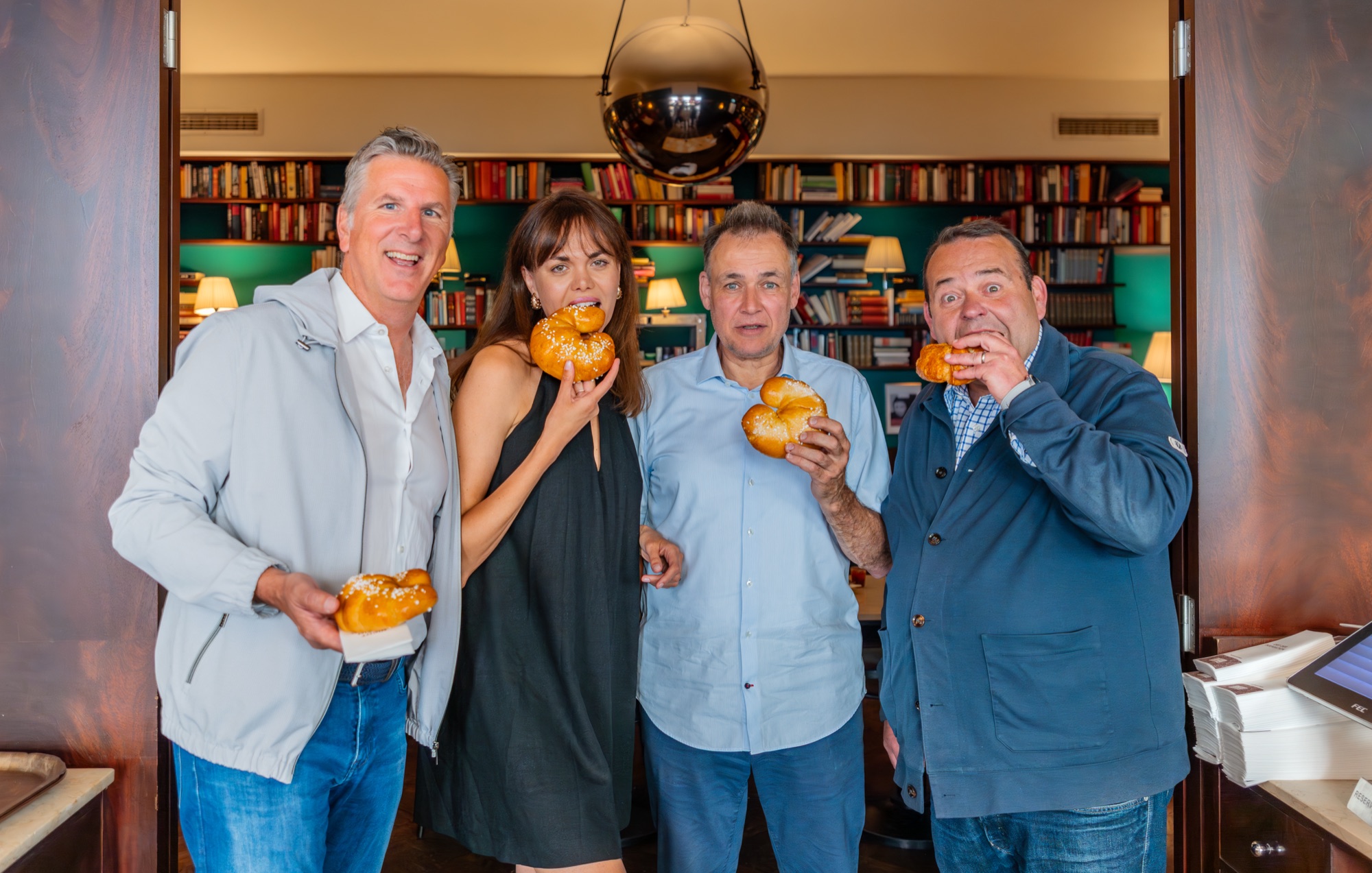 Four guests biting into fresh croissants in front of a green library bookshelf at the IMMMA event, Vienna — event photography by Best Alex Shots